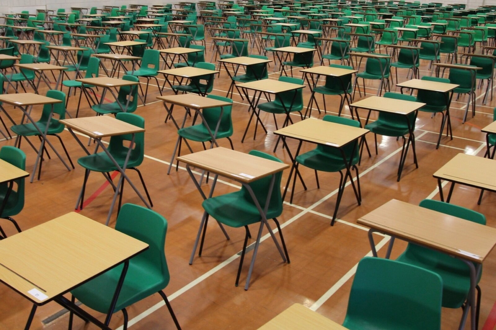 Rows of empty desks and chairs laid out in a school hall for an examination