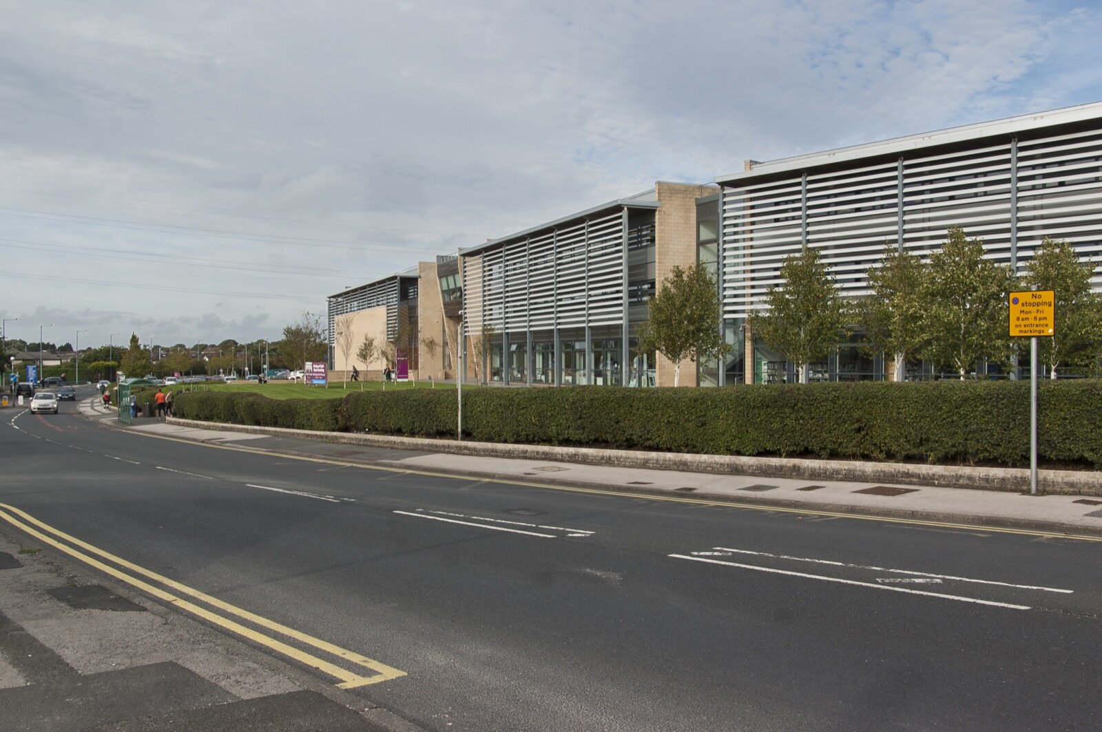 The modern main building of Blackpool Sixth Form College with louvred cladding behind a hedge and a road
