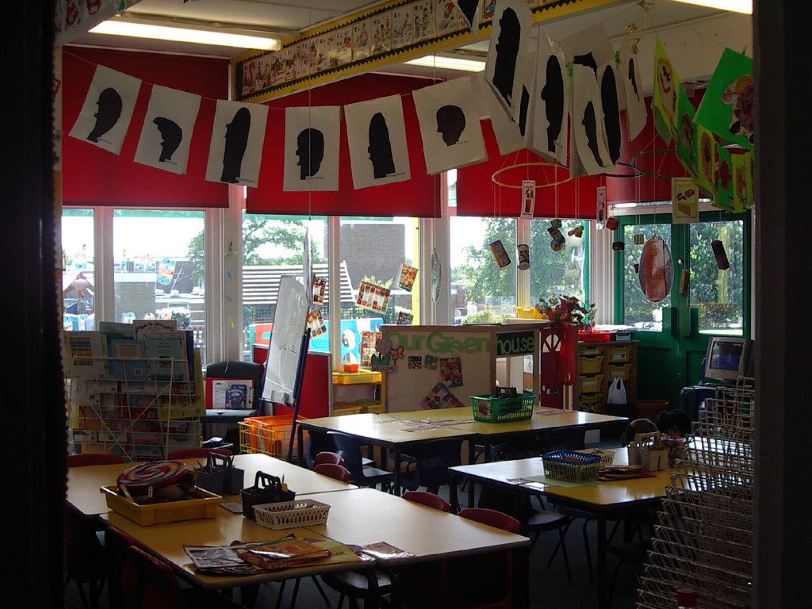 An empty reception classroom with low tables, trays of resources and children's artwork hung across the windows